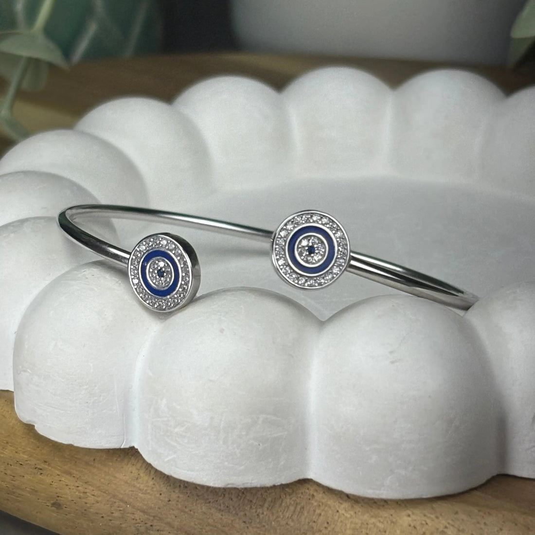 Silver bracelet with blue and white circular charms on a white shell-like surface.
