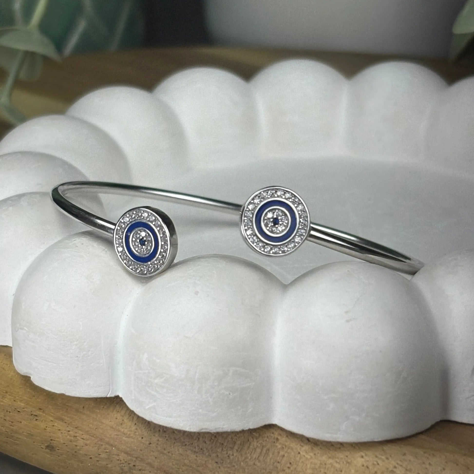 Silver bracelet with blue and white circular charms on a white shell-like surface.