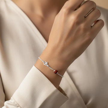 Silver bracelet with red beads on a wrist against a neutral background