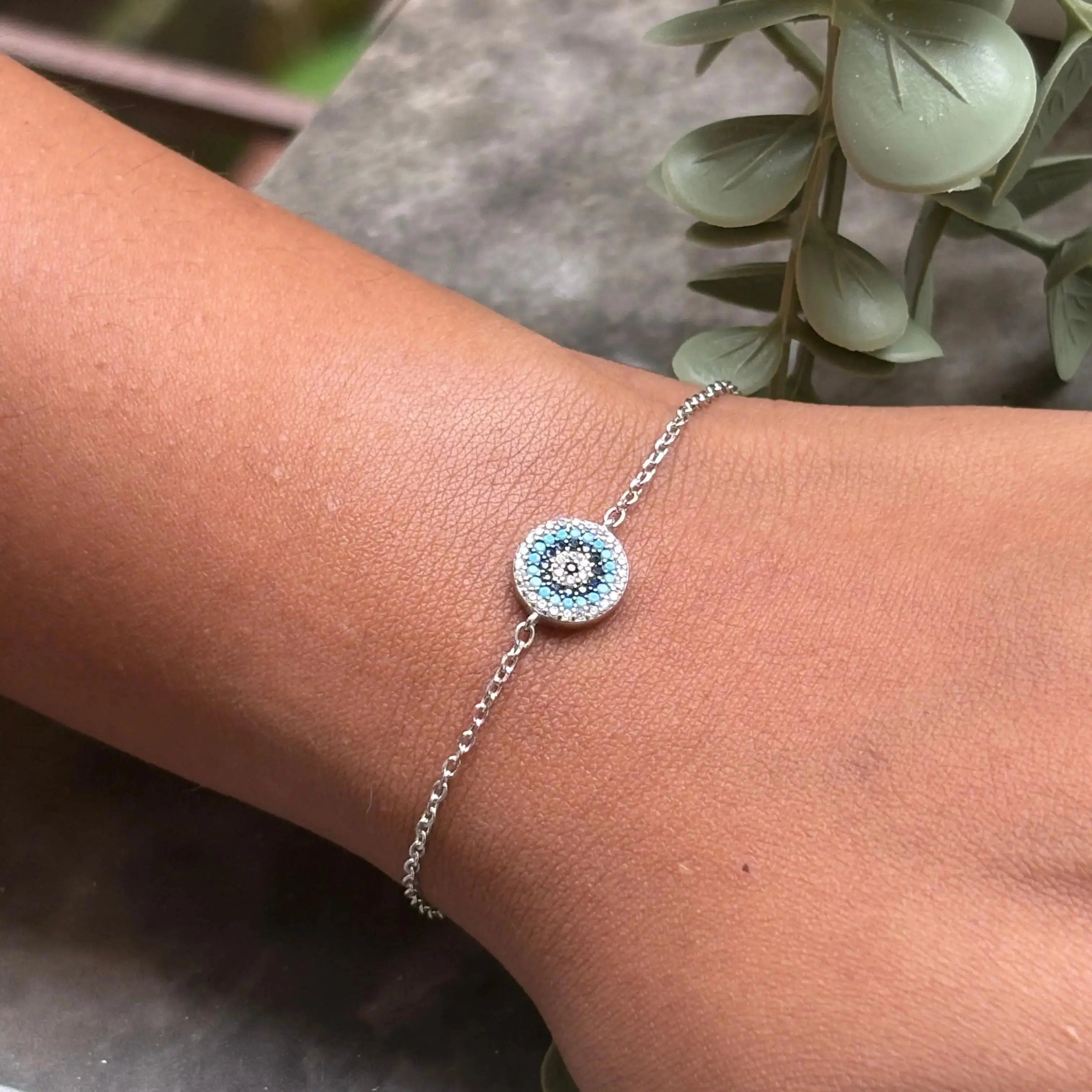 Silver bracelet with a blue and white circular design on a wrist, with green leaves in the background.