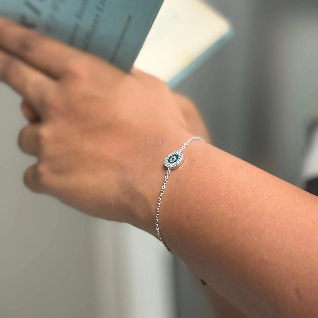 Hand wearing a silver bracelet with a blue gemstone on a light background, featuring text about the product.